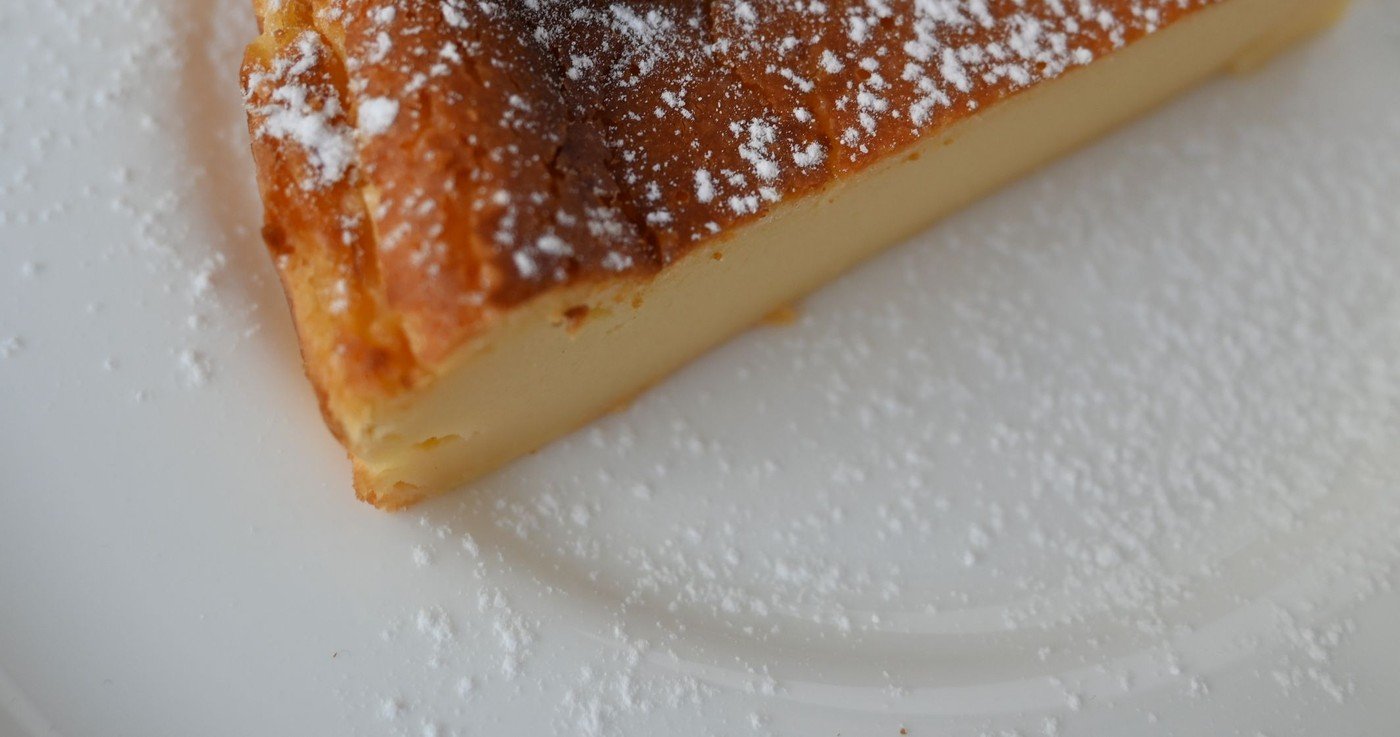A wedge of pale baked custard flan with a browned, sugar-dusted top on a white plate