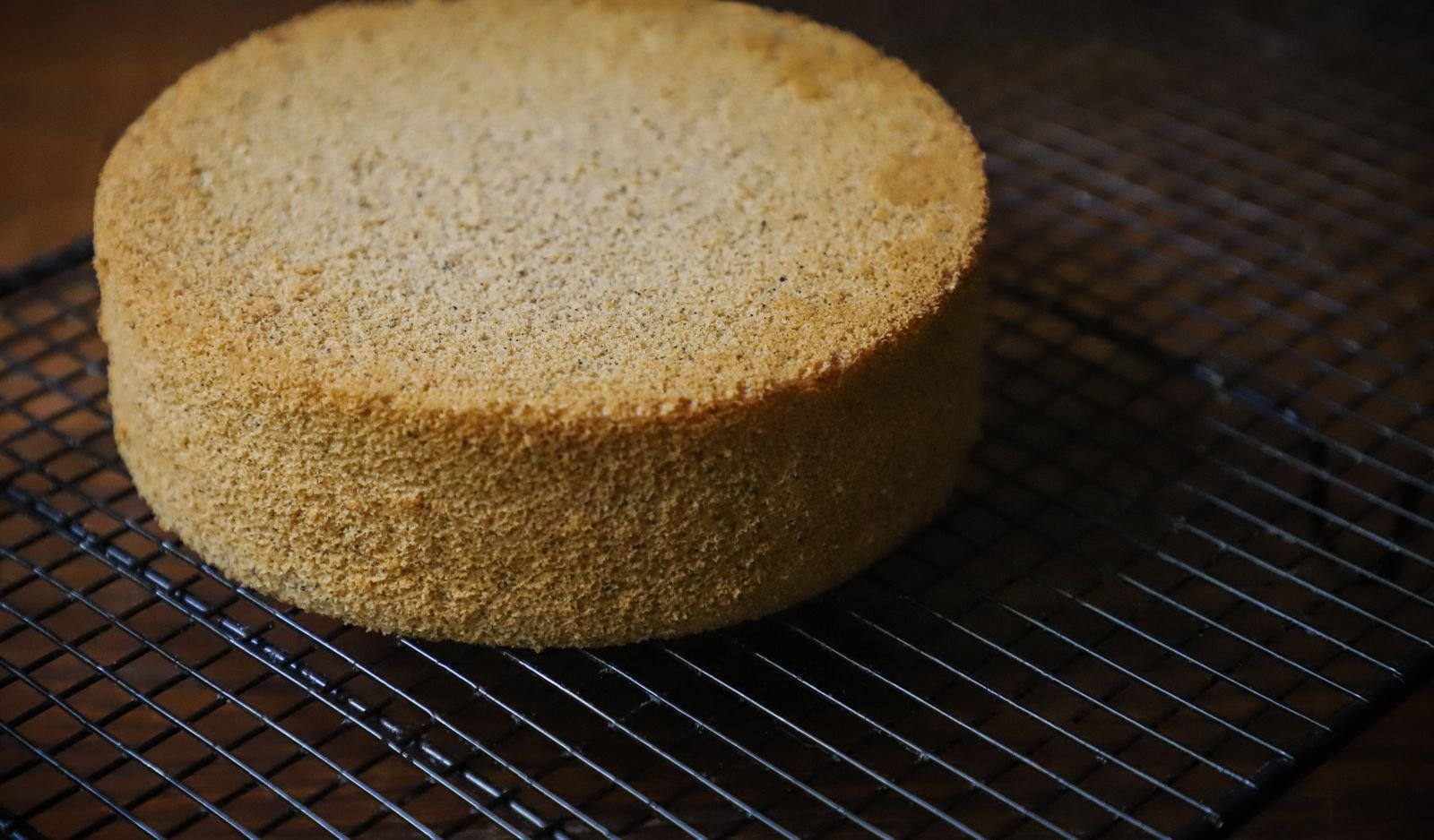 A round golden sponge cake cooling on a wire rack