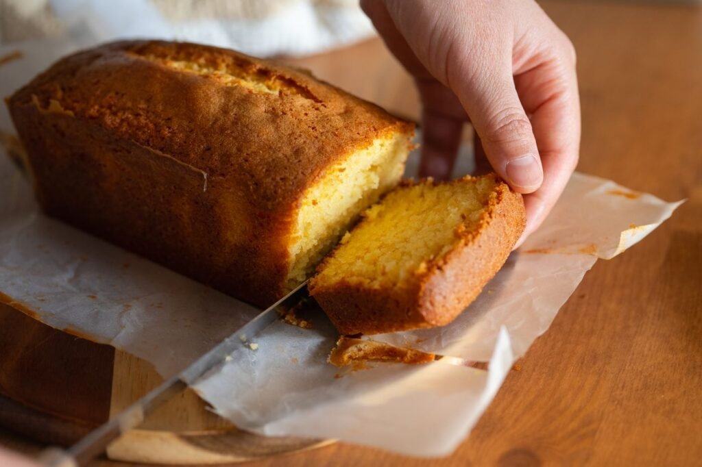 A golden loaf of pound cake being sliced on parchment
